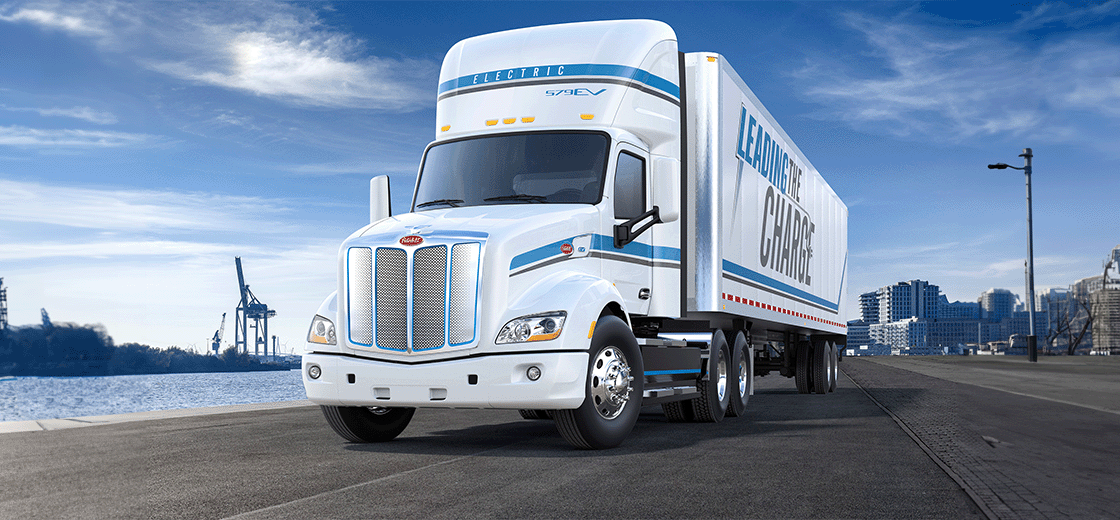 Image of two Peterbilt electric trucks parked in front of an EV charger