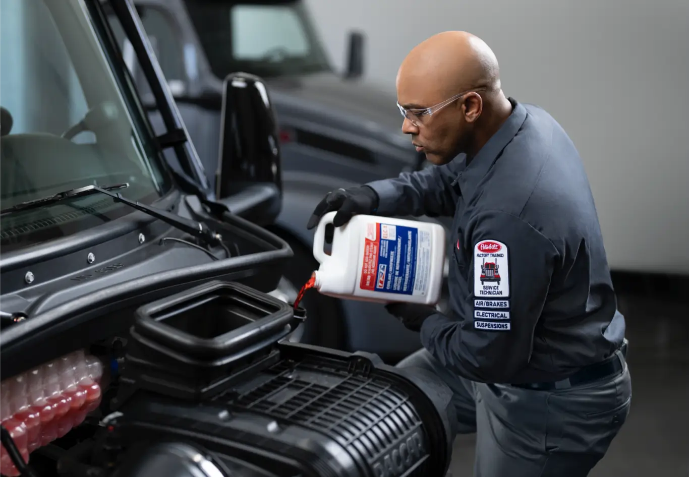 A Peterbilt technician adds coolant to a truck